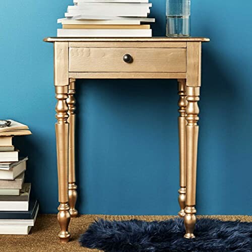 Gold side table with a drawer, stacks of books, and a glass on top.