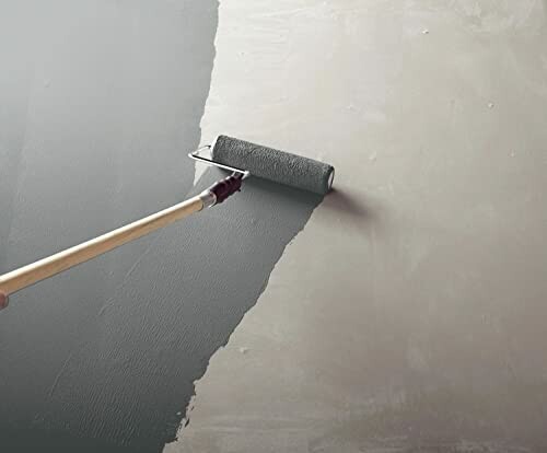 Paint roller applying dark gray paint on wall.